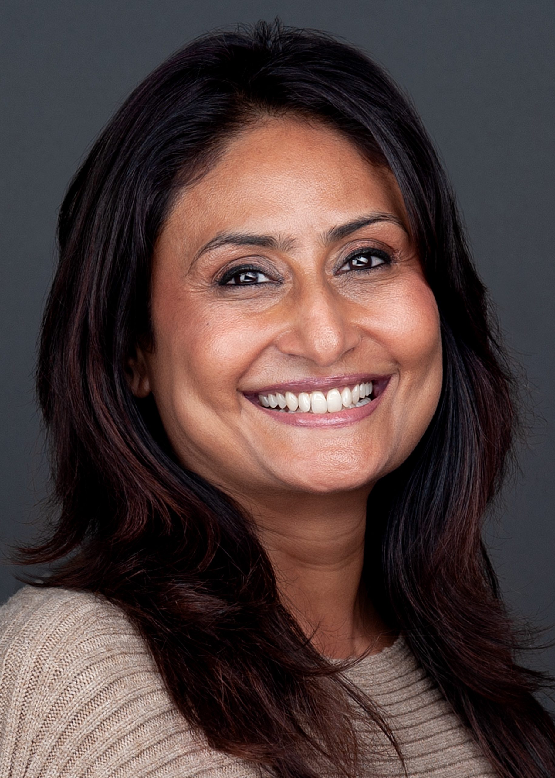 A woman in a tan sweater is captured by a professional photographer for personal branding purposes.