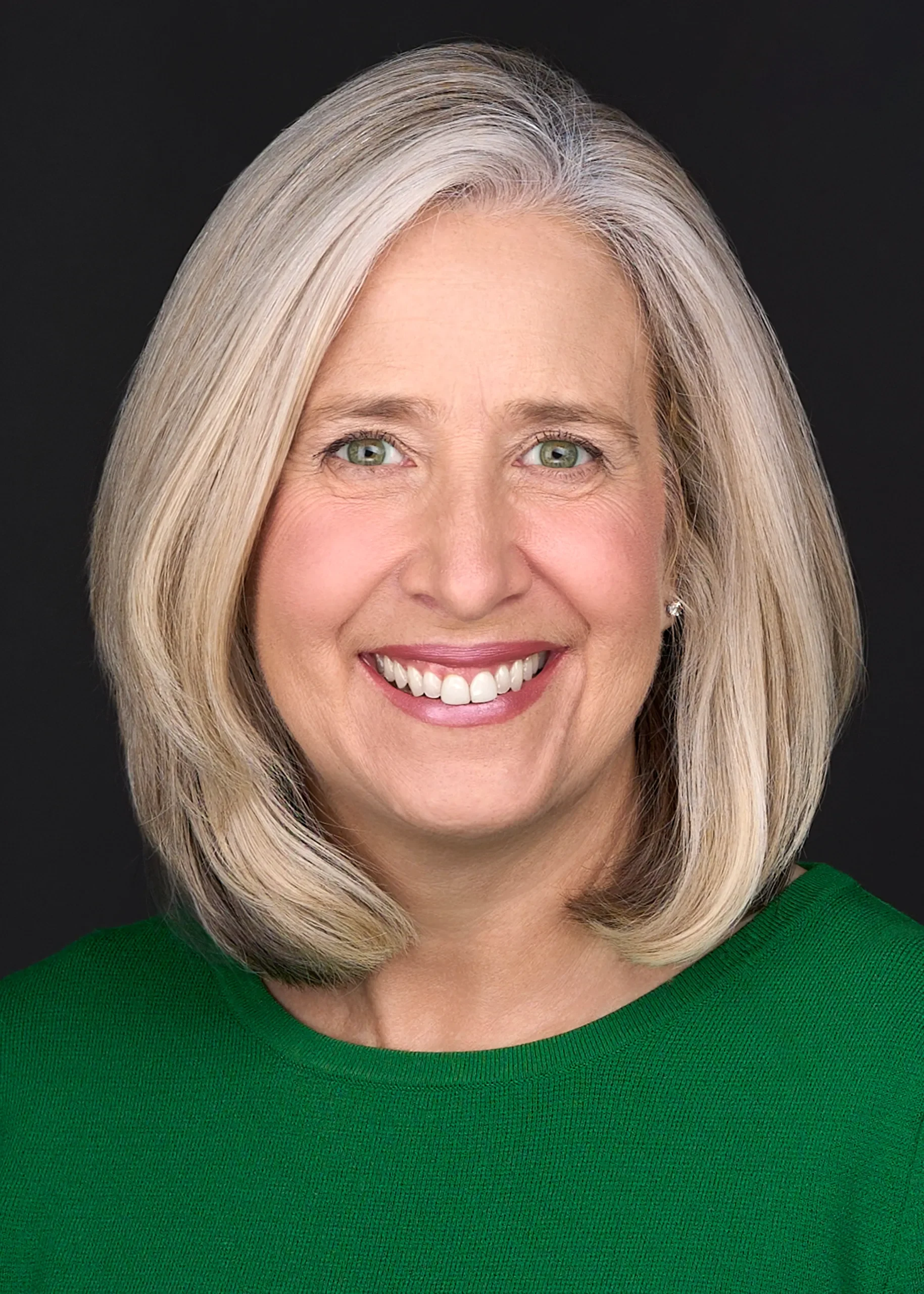 A women with gray hair and a bright green sweater smiles beautifully while posing for a professional headshot in front of a black background in Raleigh Nc